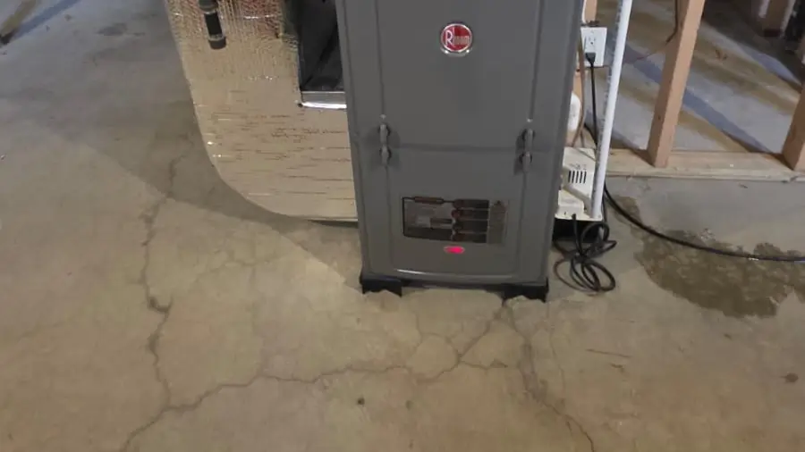 A grey gas furnace on a concrete basement floor with exhaust and intake pipes above it