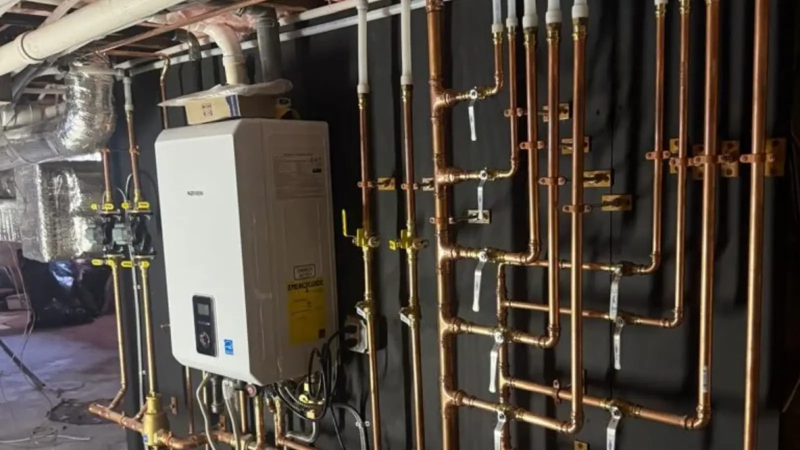 A wall of new copper water lines in a basement with a wall-mounted tankless water heater above them