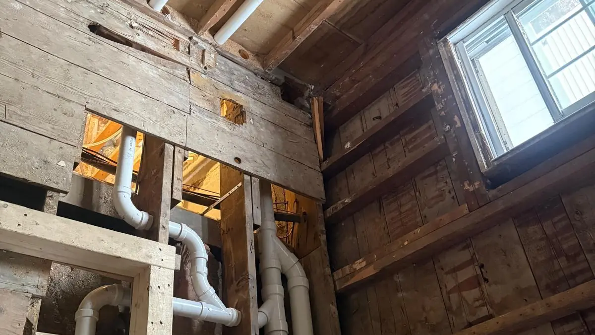 New white plastic drain piping running through the old wood framing of a house basement during a renovation