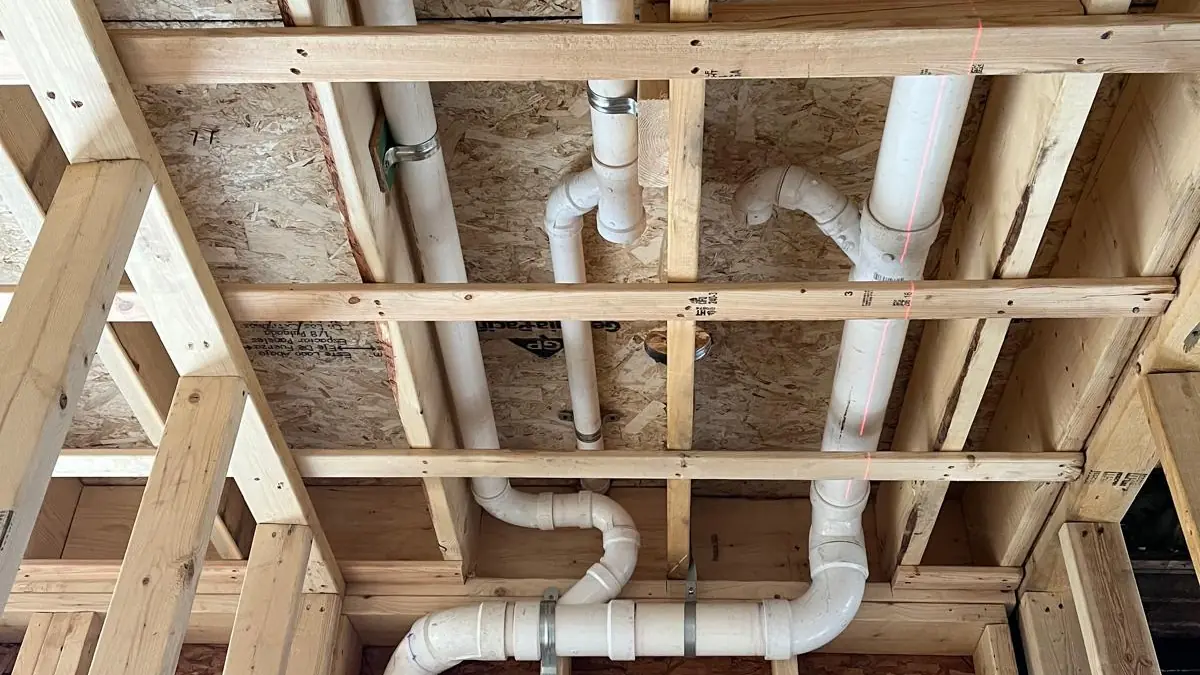 White PVC drain and vent piping running through new wood framing and an OSB subfloor during construction