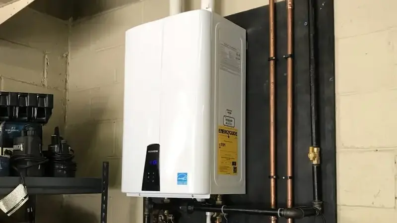 Wall-mounted tankless water heater with copper and black gas supply lines on a black backboard in a utility room