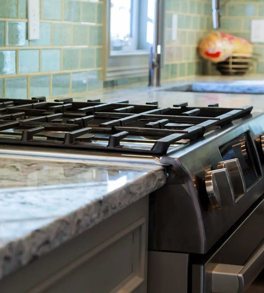 Stainless steel gas range with cast iron grates set into a granite kitchen counter