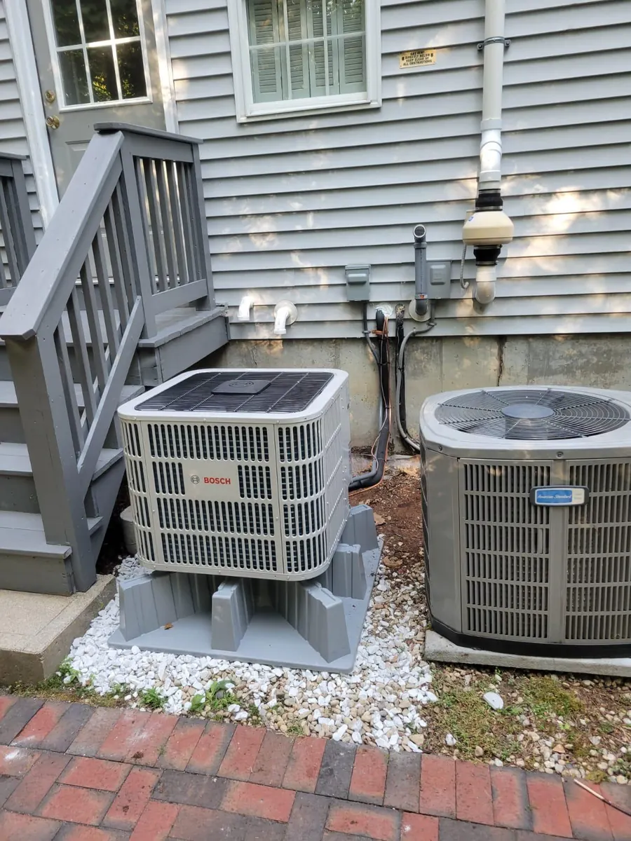 Ducted heat pump outdoor units on raised pads beside a house