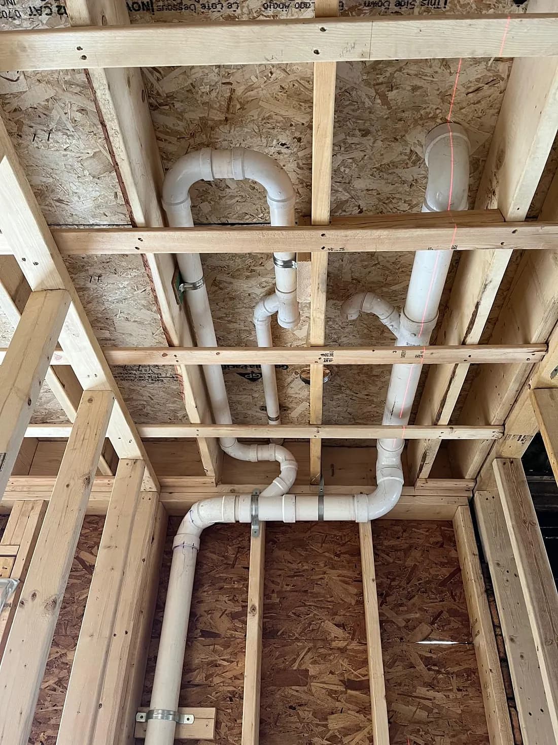 White PVC drain and vent lines running through floor joists